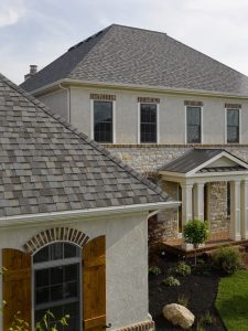 A close-up image of a GAF shingle roofing system on a modern home with stucco siding.
