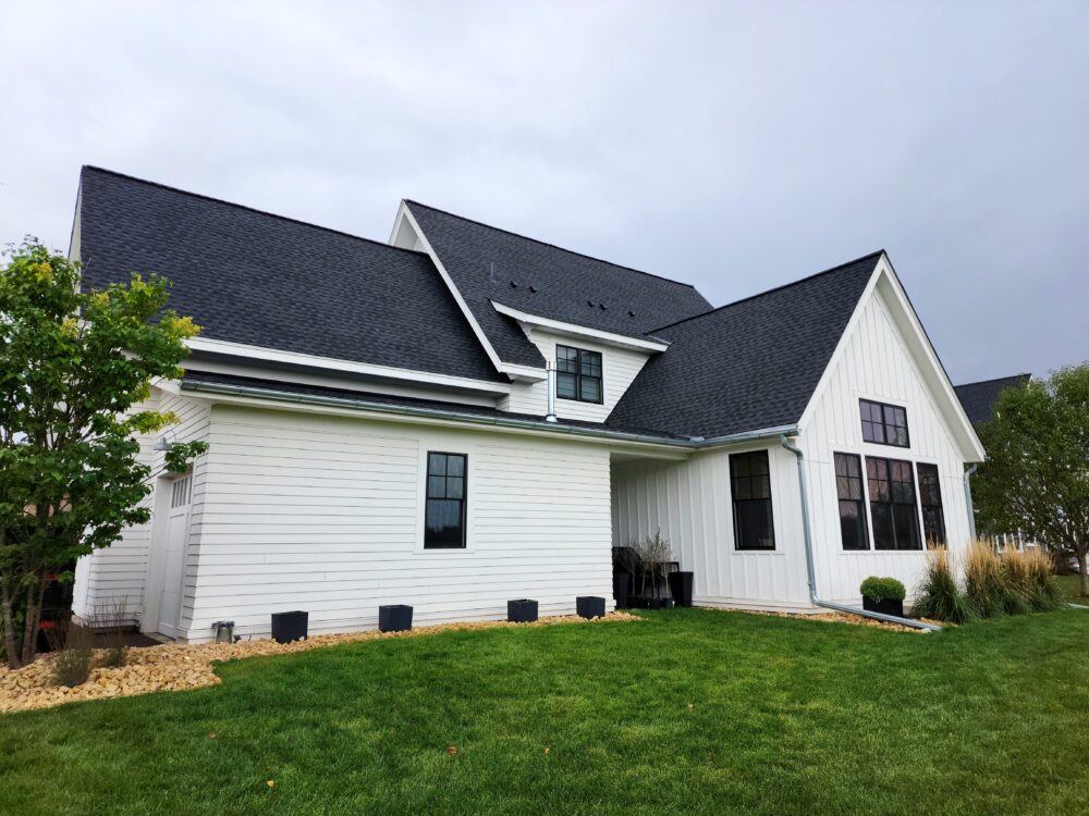 Modern farmhouse exterior featuring white board and batten siding, a black roof, and window frames by window contractors in Minneapolis, MN