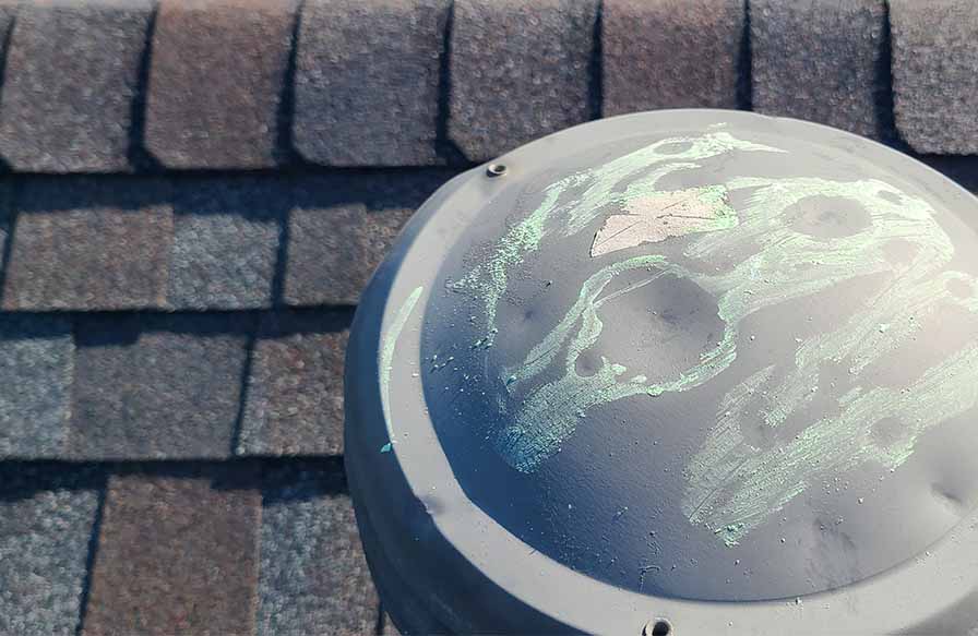 A close-up of a gray roof vent on a shingled roof that had roof hail damage in Minneapolis, MN