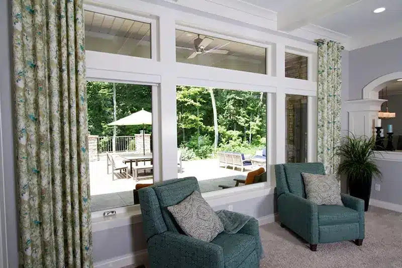 A bright living room with large provia windows offering a view of a patio and wooded area in Minneapolis, MN