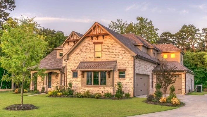 Two-story stone house with multiple gables, varied rooflines, attached garages, and professionally landscaped grounds by Wright at Home Roofing & Exteriors in Minneapolis, MN