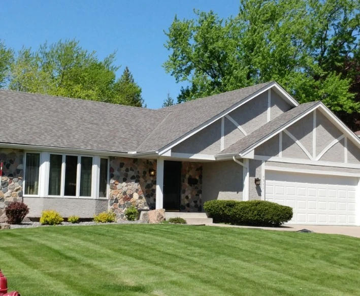 Exterior view of a home featuring a gray roof, a stone accent wall, stucco siding that had a storm damage repair in Minneapolis, MN