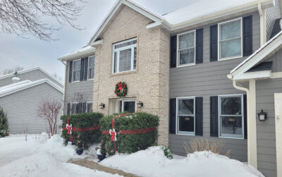 A snow-covered two-story house with fiber cement siding and a brick facade sits elegantly at Wright at Home Roofing & Exteriors Minneapolis, MN.