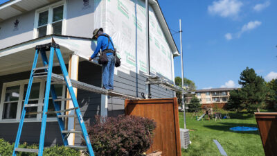 A worker on a ladder diligently installs James Hardie siding on a two-story home at Wright at Home Roofing & Exteriors Minneapolis, MN