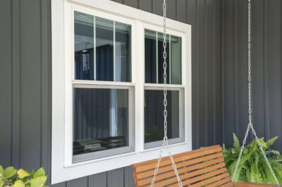 A wooden porch swing hangs by chains in front of ProVia windows with white trim on a dark gray paneled wall Wright at Home Roofing & Exteriors Minneapolis, MN