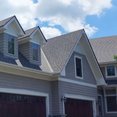 A two-story house with light gray siding, a dark gray shingle roof, and two dormer windows installed by a residential roofing contractor in Minneapolis, MN