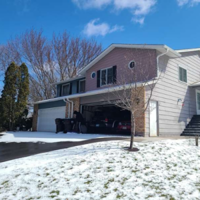 A two-story house with light gray siding with a garage and patches of snow on the ground by siding contractor in Minneapolis, MN