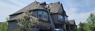 A crew of workers are on a ladder and the roof of a two-story house, replacing the roof shingles in Minneapolis, MN