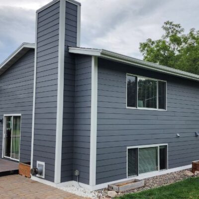 A two-story house with dark gray lap siding and white trim, featuring a chimney and sliding glass doors leading to a patio in Minneapolis, MN