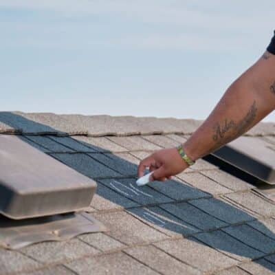 A residential roofing contractor on a ladder on top of a roof in a process of roof inspection for roof repair minneapolis, MN