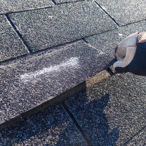 Professional inspector examining a residential shingle roof for signs of what storm damage looks like, using a white marking tool by Wright at Home Roofing & Exteriors in Minneapolis