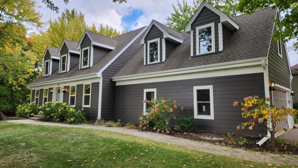 Contemporary house with gray siding, white trim, a brown roof, and a covered porch by roofing and siding contractors in Minneapolis, MN