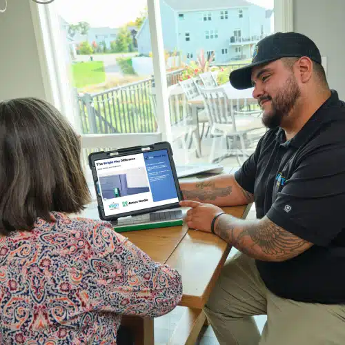 Roofing specialist presenting a detailed proposal on a laptop to a homeowner at a dining table, illustrating how to compare roof estimates—scope, materials, timelines, and warranties—by Wright at Home Roofing & Exteriors in Minneapolis
