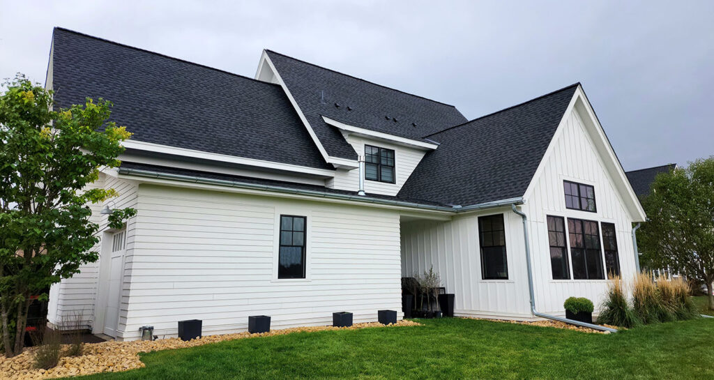 A modern white house with dark gray shingles, showcasing two peaked roofs and large windows Wright at Home Roofing & Exteriors in Minneapolis, MN.