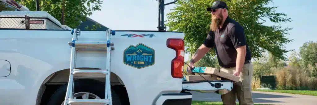 Wright at Home Roofing & Exteriors team member unloading roofing materials from branded work truck at a residential job site