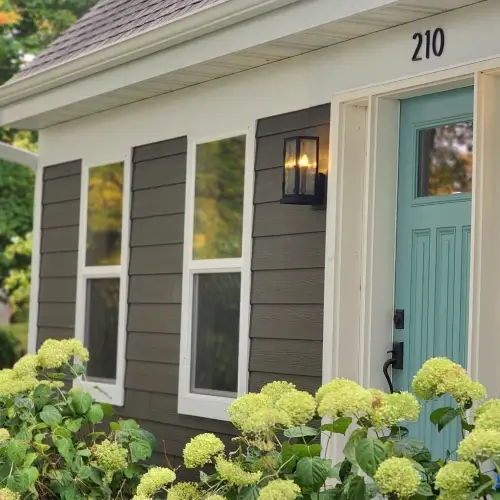 Home with modern gray siding, teal front door, new windows, and blooming hydrangea bushes, showing exceptional results and roofing company reviews Minneapolis by Wright at Home Roofing & Exteriors