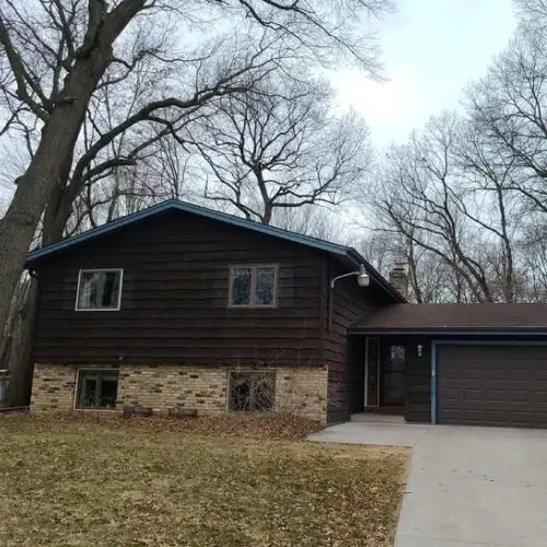 Minneapolis split-level home with dark brown wood siding, blue trim, brick lower accent, and two-car garage—featured for siding visualizer by Wright at Home Roofing & Exteriors