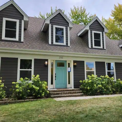 Split-level home in Minneapolis with dark brown horizontal siding, white trim, teal front door, and manicured hydrangea bushes—example created using the siding visualizer by Wright at Home Roofing & Exteriors