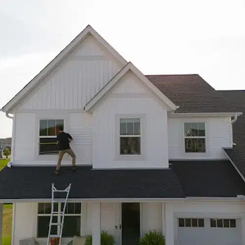 Roofer on ladder inspecting upper-level roof for storm damage by Wright at Home Roofing & Exteriors in MN