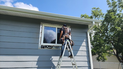 Roofing contractor performing window repair on blue house exterior by Dolan Roofing & Construction in Robbinsdale, MN