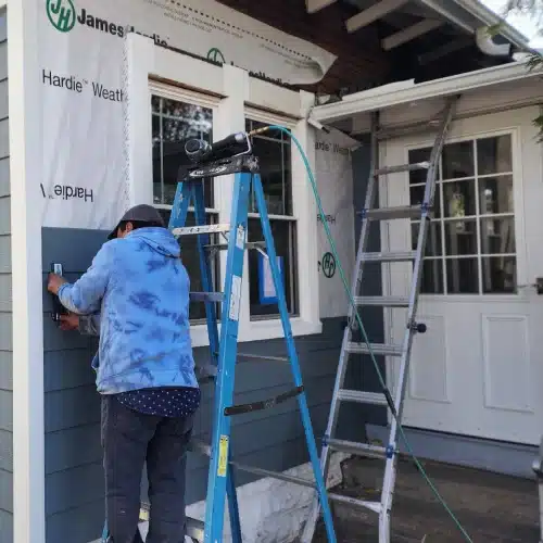 Siding expert installing durable blue Hardie board panels on Minneapolis home exterior by Wright at Home Roofing & Exteriors