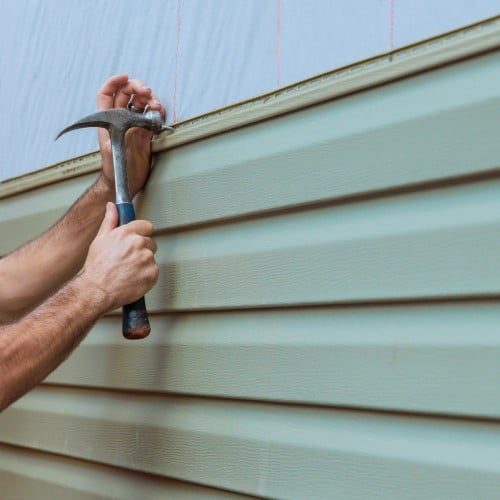 Contractor installing green siding panel using a hammer during siding installation by Wright at Home Roofing & Exteriors in Minneapolis