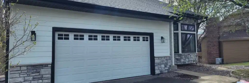 Home exterior restoration in Plymouth, MN with James Hardie siding, black trim, stone veneer, and a new garage door with windows by Wright at Home Roofing & Exteriors in Plymouth, MN