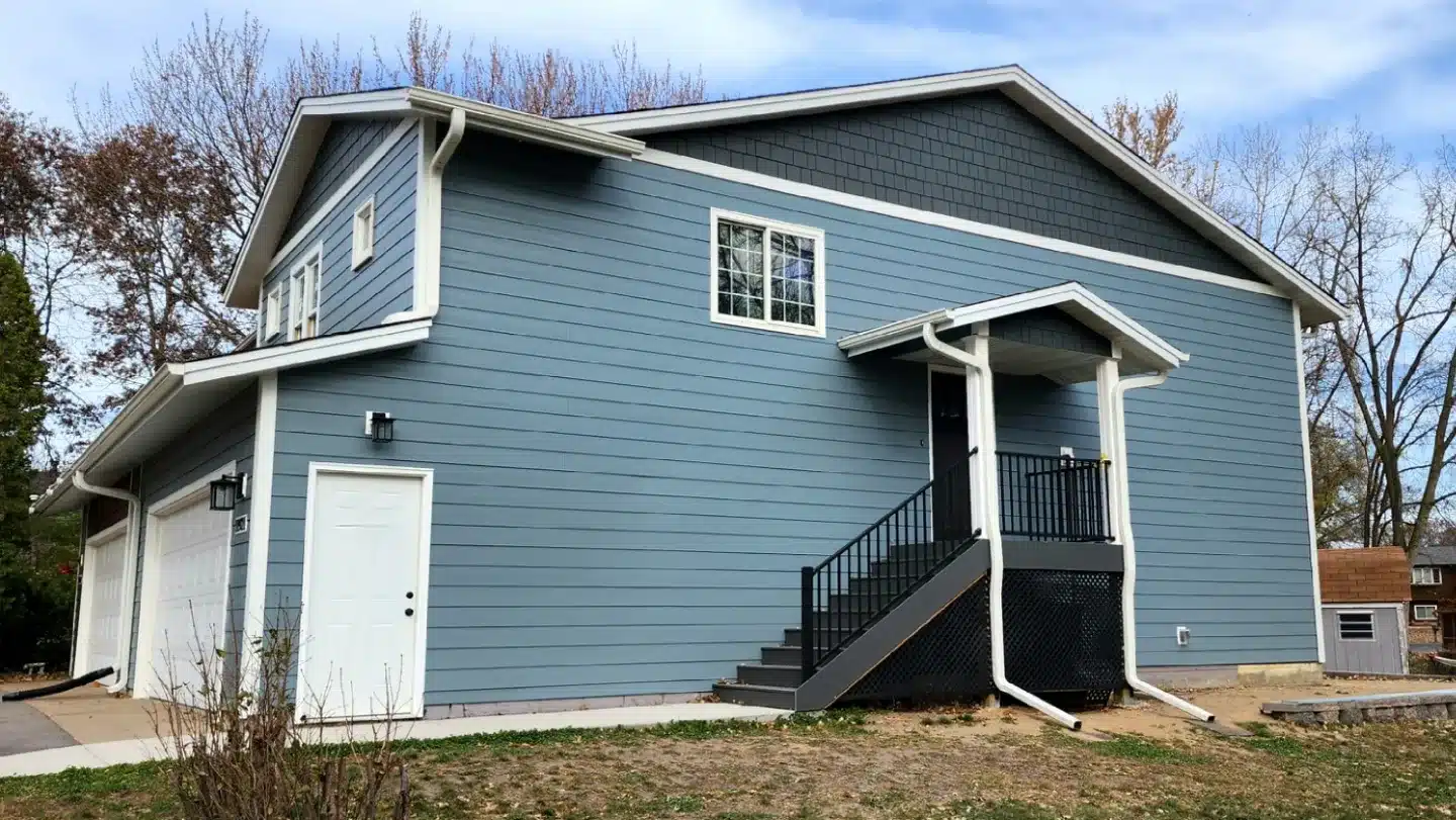 Two-story blue-gray home featuring dark gray shake siding in the upper gable and fresh white-framed windows, highlighting a completed project to replace siding and windows together in Blaine, Minnesota by Wright At Home